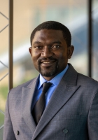 A man with short dark hair wearing a dark blue suit and tie.