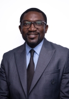 A man with short dark hair wearing glasses and a dark blue suit and tie.