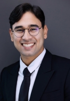 A person with short black hair wearing glasses and a suit and tie.