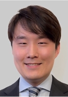 Smiling man with short black hair wearing a dark suit and tie.