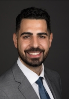 Smiling man with a short black beard and hair wearing a suit and tie.