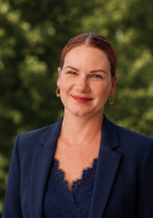 woman in blue blazer in front of trees