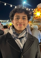 Smiling person with short black curly hair wearing a coat and scarf.
