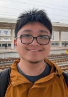 Smiling person with short spiky black hair wearing glasses and an orange jacket.