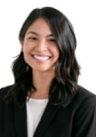 Smiling person with long black hair wearing a black jacket over a white top.