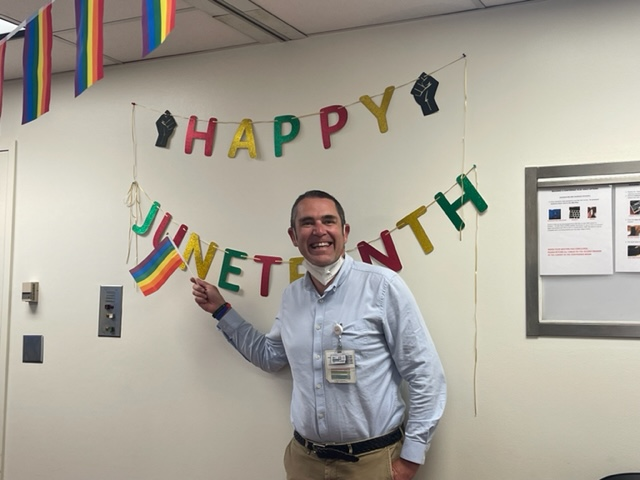 Romain Pirracchio, MD, PhD, chief of Anesthesia at ZSFG, waves a Pride flag in front of a Happy Juneteenth banner